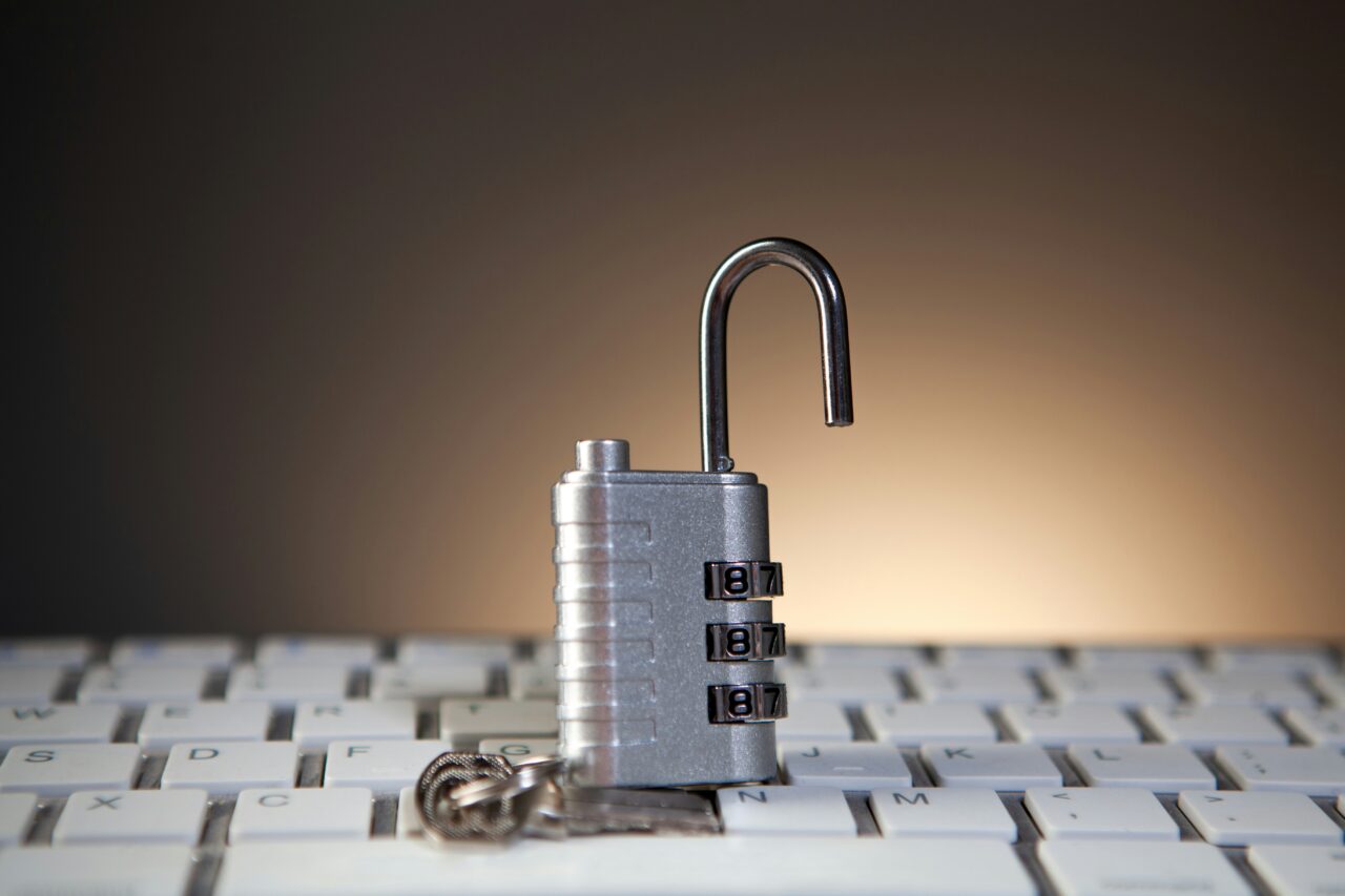 Open silver combination padlock standing on a white computer keyboard.