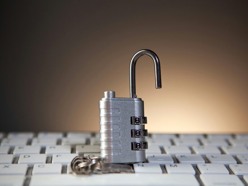Open silver combination padlock standing on a white computer keyboard.