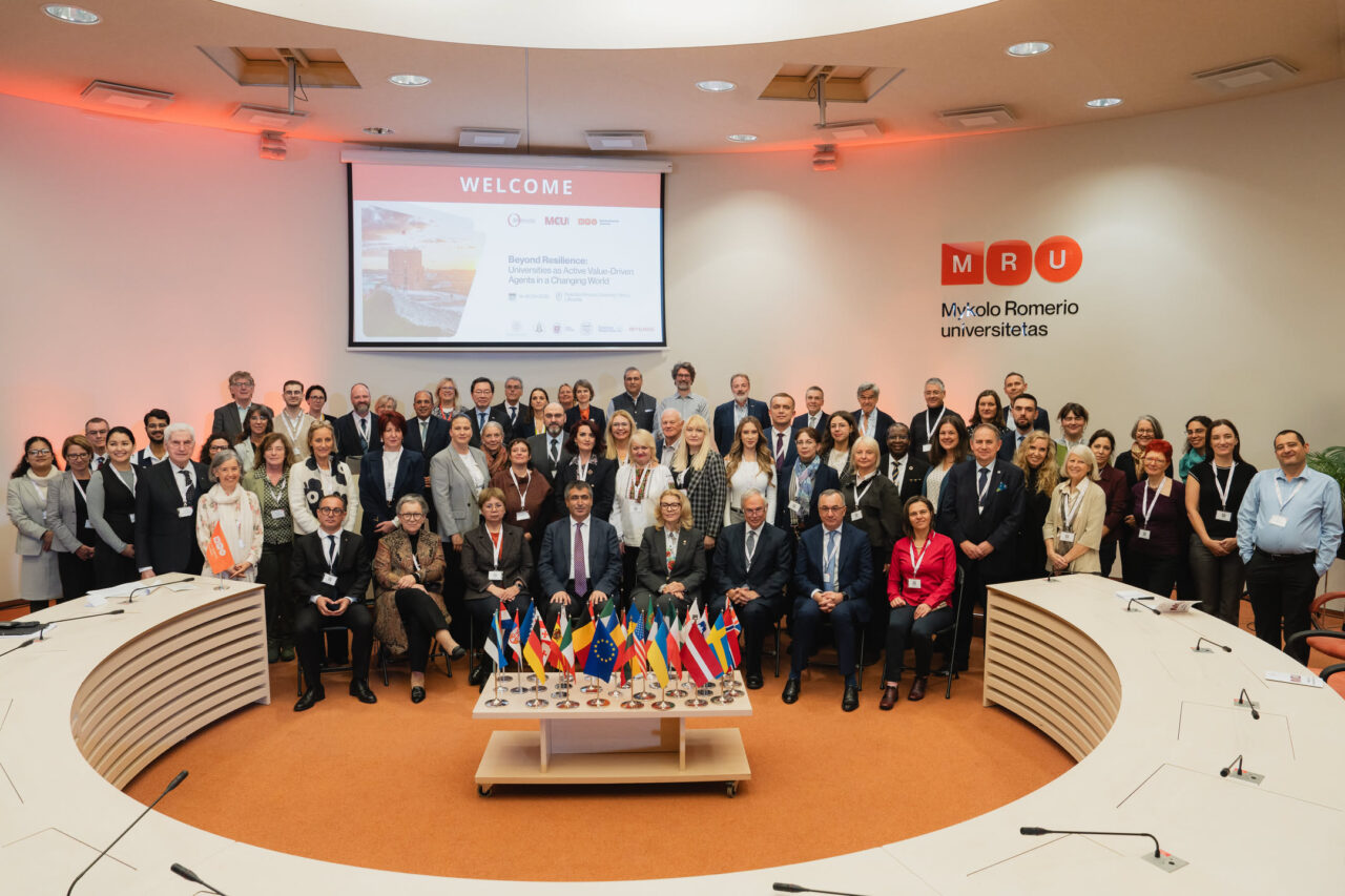 Participants pose for a group photograph behind a display of national flags at Mykolas Romeris University.