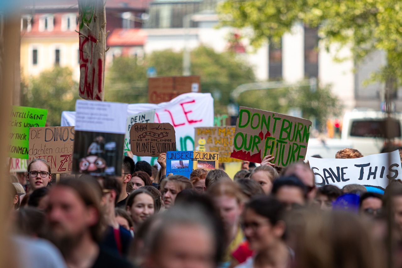 A crowded climate demonstration with protesters holding hand-painted placards displaying messages in different languages, including “DON’T BURN OUR FUTURE” and “UNSERE ZUKUNFT”.