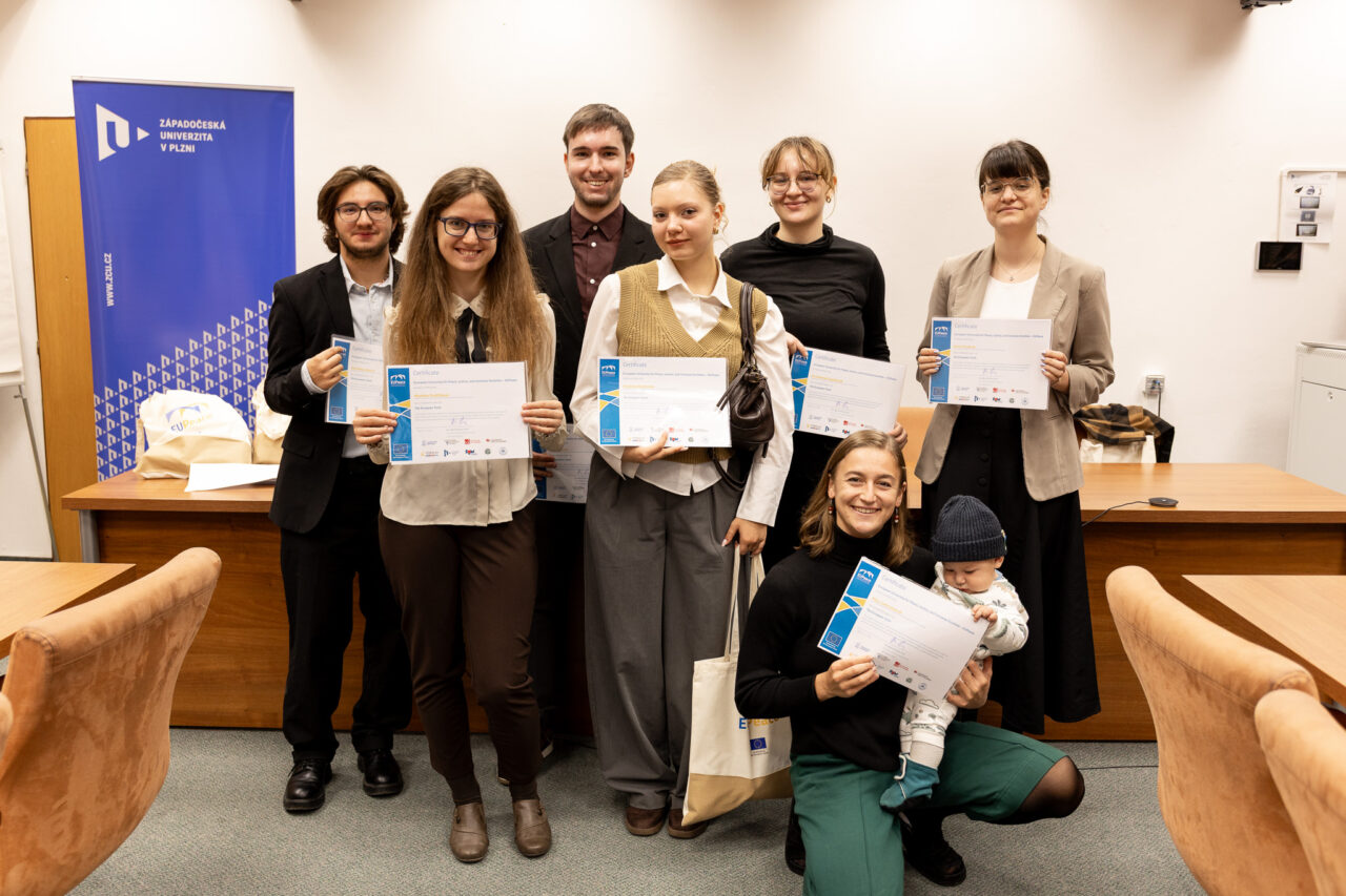 Seven students at the University of West Bohemia in Pilsen holding their newly earned European Track certificates. They are standing in front of a wooden desk, with a UWB roll-up banner in the background.