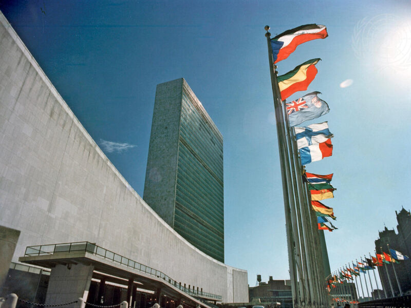 United Nations Headquarters in New York, featuring the Secretariat Building and a row of international flags against a clear blue sky.