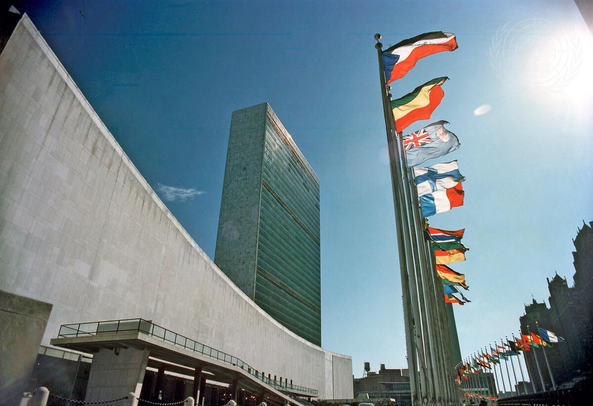United Nations Headquarters in New York, featuring the Secretariat Building and a row of international flags against a clear blue sky.