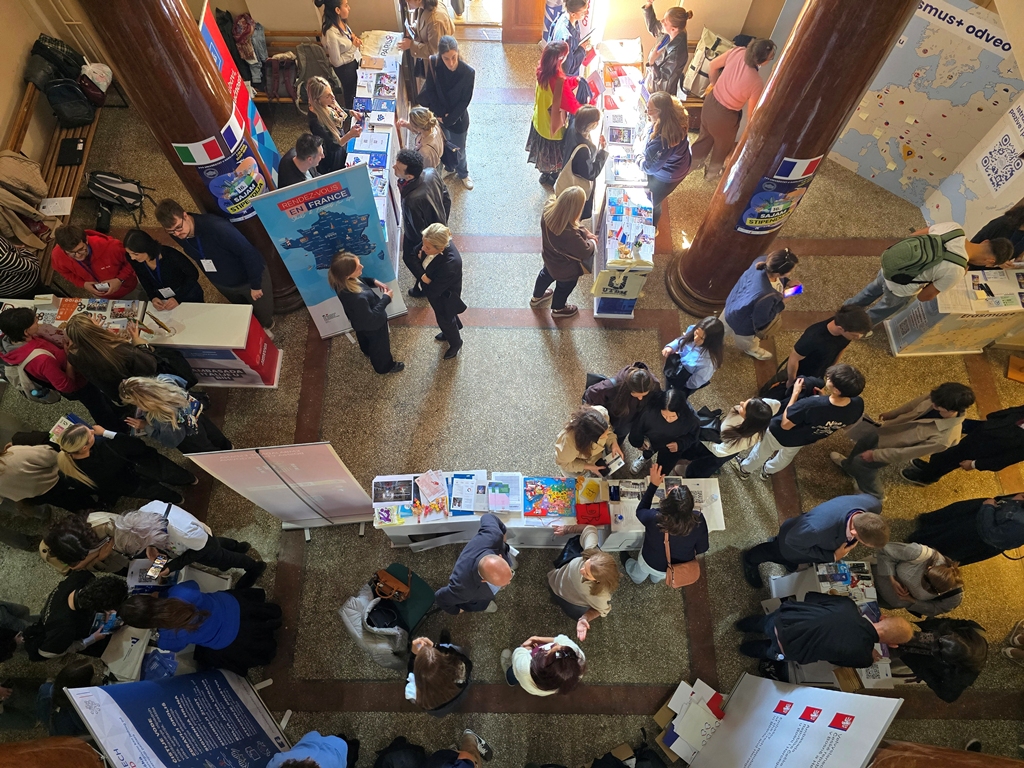 Aerial view of students and staff moving between exhibition stands in a hall with marble columns.