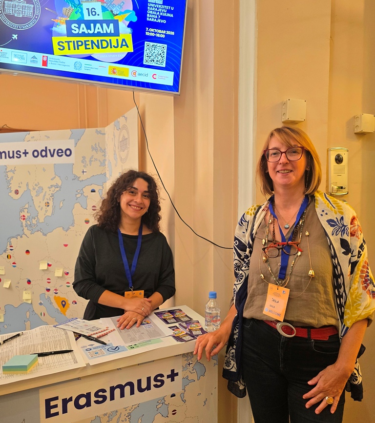 Two smiling women at an Erasmus+ stand with a map of Europe, below a screen announcing the 16th Scholarship Fair.