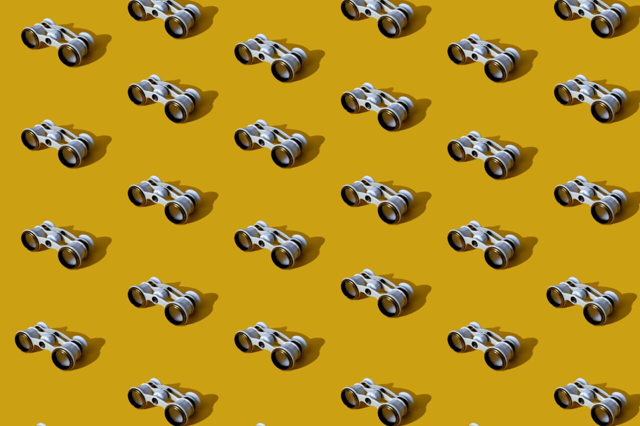 A repeating pattern of small white and silver opera glasses with long shadows on a mustard-yellow background.