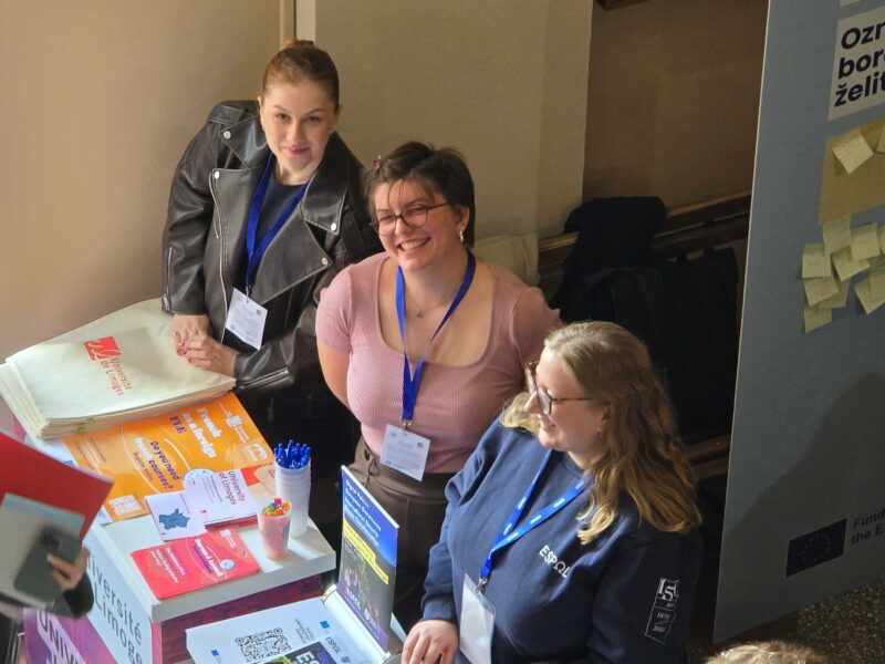Three university representatives stand behind a University of Limoges information stand displaying brochures, promotional materials and university information.