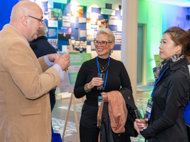 Three conference participants converse over refreshments beside research displays at ICES 2026.