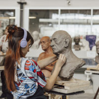 Participants at ArtCamp sculpt life‑size clay head studies during a clay modelling course.