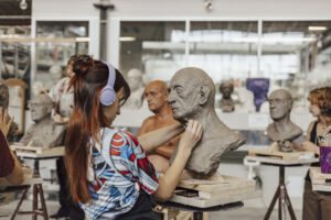 Participants at ArtCamp sculpt life‑size clay head studies during a clay modelling course.