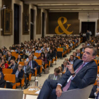 Margaritis Schinas speaks at Comillas Pontifical University during the presentation of the Chair on Strategic Autonomy Studies, with attendees and speakers visible in the background.