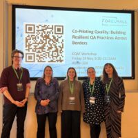 One man and four women posing in front of a projector wall for a group picture. The four persons are the workshop moderators for a workshop on Quality Assurance at the European Quality Assurance Forum 2025