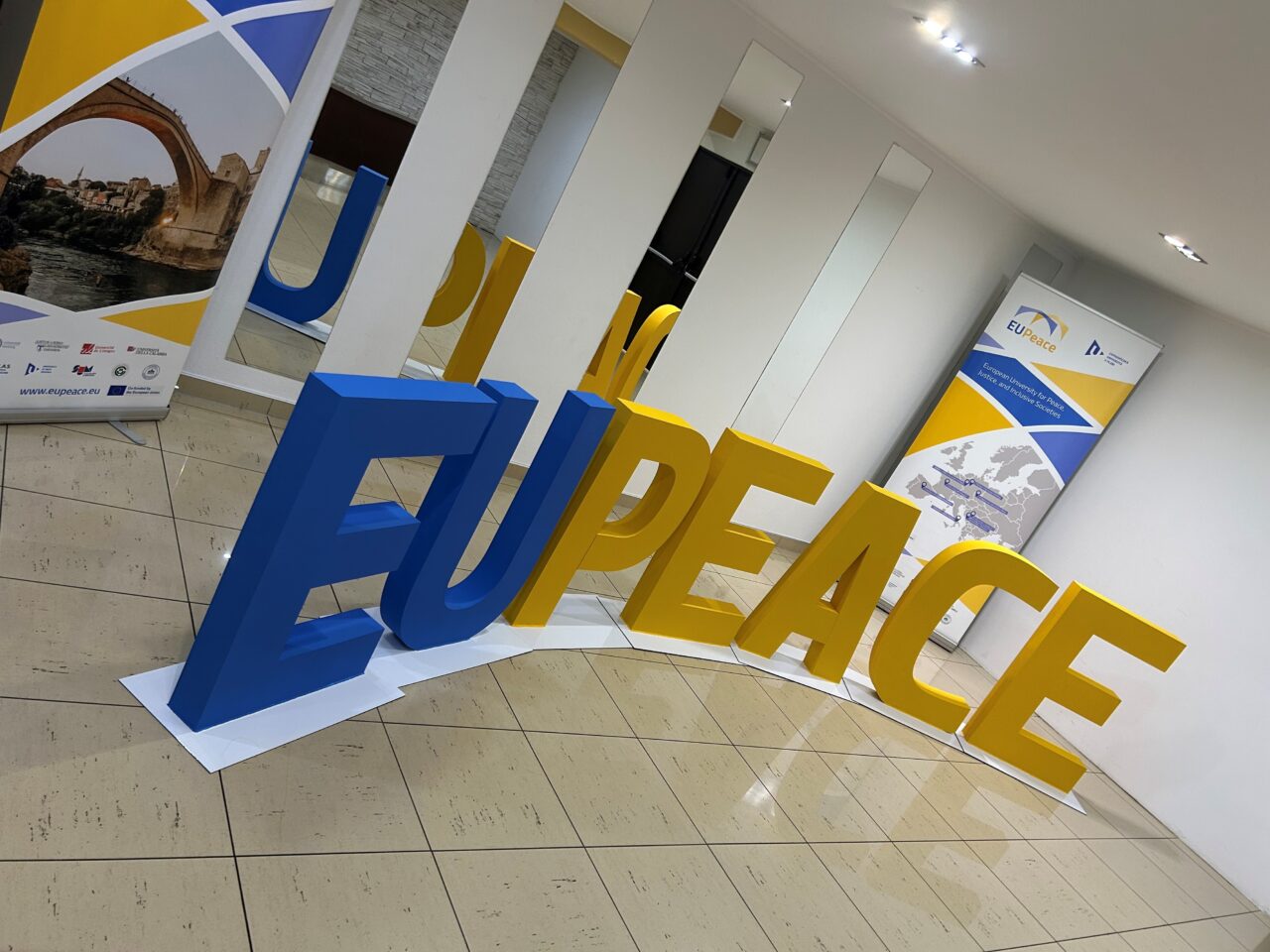 Large 3D letters spelling "EUPeace" in blue and yellow displayed at the EUPeace Autumn Meetings 2025 in Pilsen, Czechia, with banners showing the alliance’s mission and partner universities.