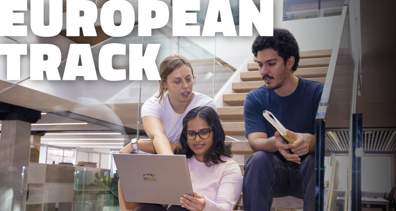 Three students sit together on a wooden staircase in a modern building with glass railings. In the middle, a student with glasses holds a laptop with the EUPeace logo on its lid, while a student behind her points at the screen and a student on the right holds a notebook. Large white letters at the top left read "European Track".