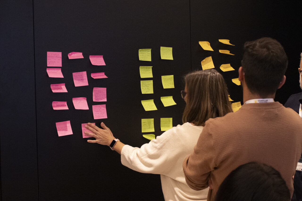 Participants place colorful Post‑its on a wall during a collaborative workshop activity.