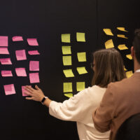 Participants place colorful Post‑its on a wall during a collaborative workshop activity.