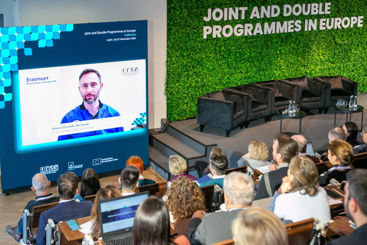 A panelist appearing on a screen via video call. Attendees listen attentively