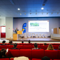 A man standing on the left side of a stage giving the keynote speech for the conference.