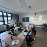 Small group discussion in a classroom setting, with people seated around tables.