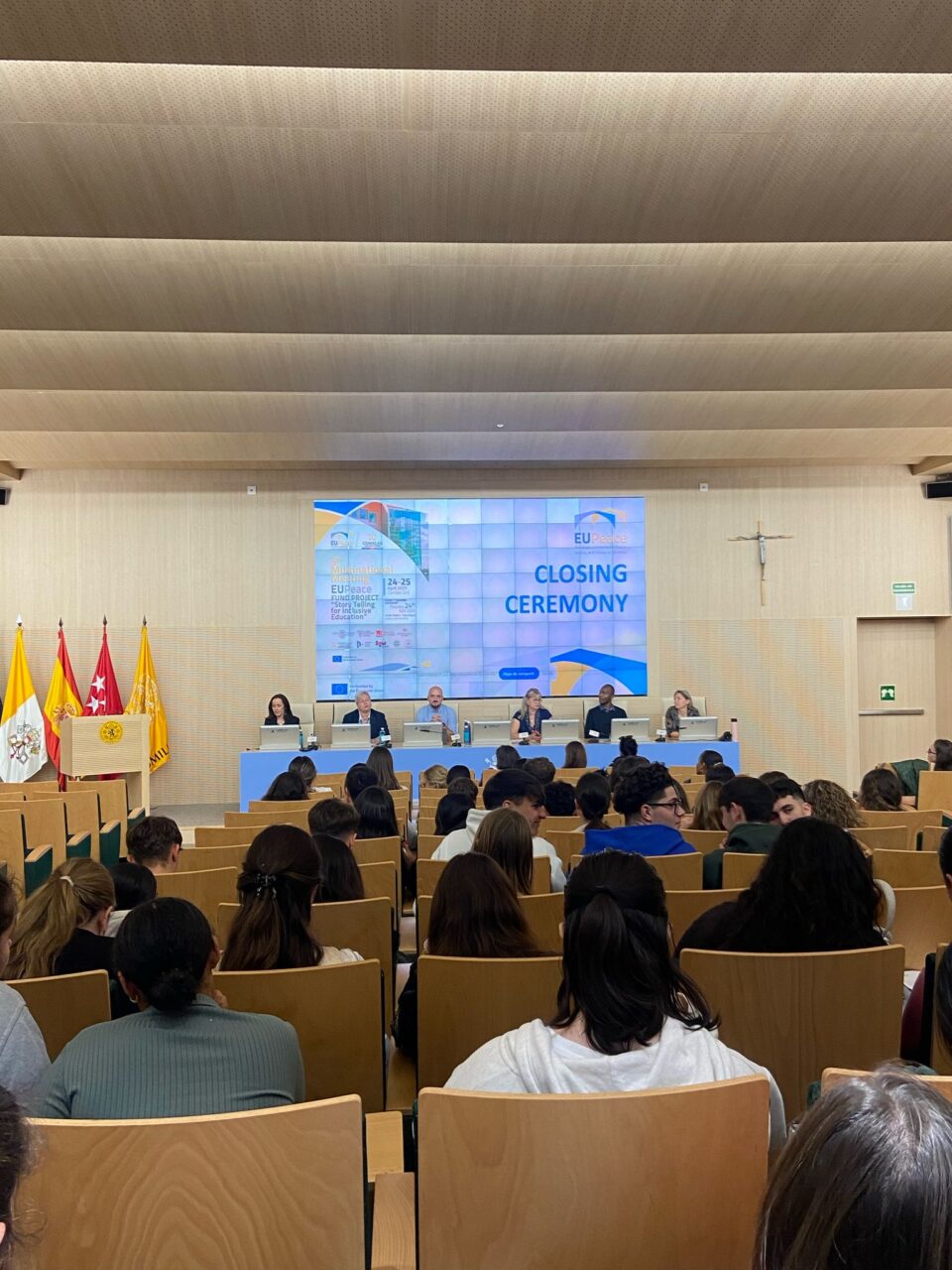 Audience seated in a university lecture hall facing a panel of speakers during the EUPeace closing ceremony, with event branding displayed on a large screen.