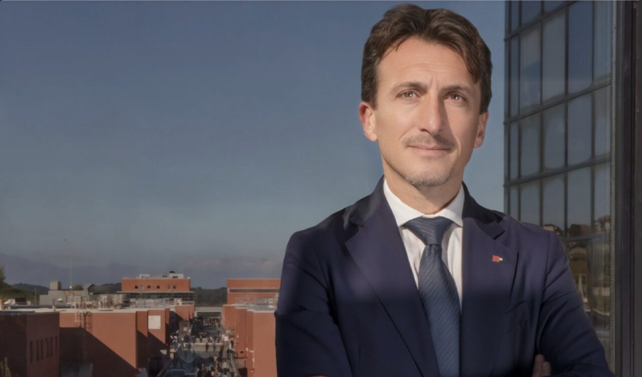 A man standing on a balcony with red square buildings behind him. The man is Gianluigi Greco, new rector at UNICAL.
