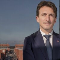 A man standing on a balcony with red square buildings behind him. The man is Gianluigi Greco, new rector at UNICAL.